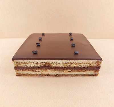 Tarta Ópera cuadrada para varias personas, fotografiada en ángulo de 45 grados, con cobertura de chocolate, cortes limpios donde se aprecian todas las capas y granos de café decorativos en la superficie.