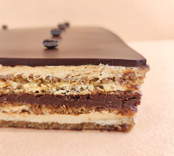 Primer plano de una Tarta Ópera cuadrada, resaltando la textura del glaseado chocolate, la suavidad de la crema de café, la cremosidad de la ganaché de chocolate y la esponjosidad del bizcocho gioconda empapado en café.