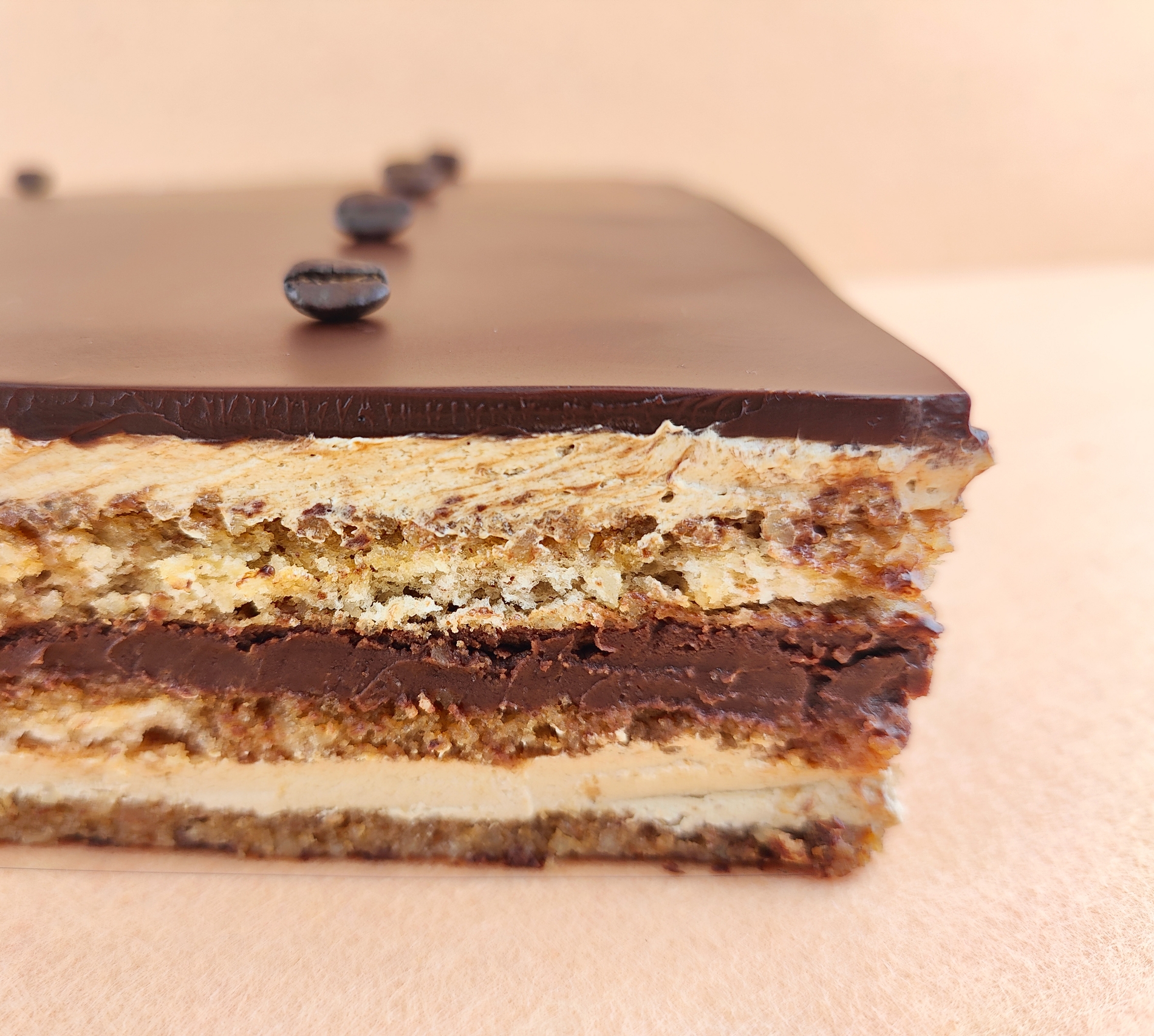 Primer plano de una Tarta Ópera cuadrada, resaltando la textura del glaseado chocolate, la suavidad de la crema de café, la cremosidad de la ganaché de chocolate y la esponjosidad del bizcocho gioconda empapado en café.