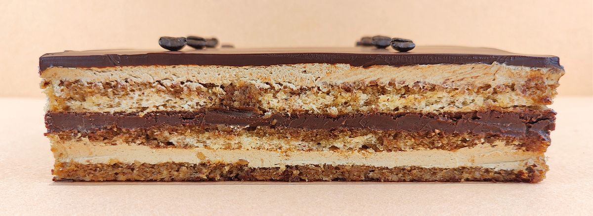 Porción individual rectangular de Tarta Ópera vista de frente, con sus capas alternas de bizcocho de almendra, crema de café y ganache de chocolate perfectamente alineadas.