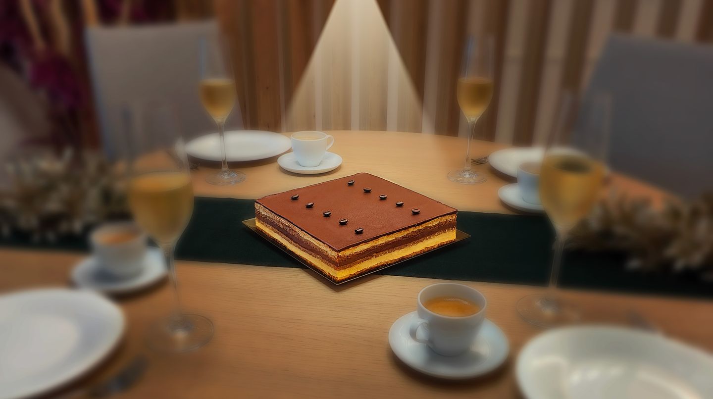 Tarta Ópera cuadrada iluminada por un foco teatral sobre una mesa con vajilla de postre, inspirada en una escena de ópera.