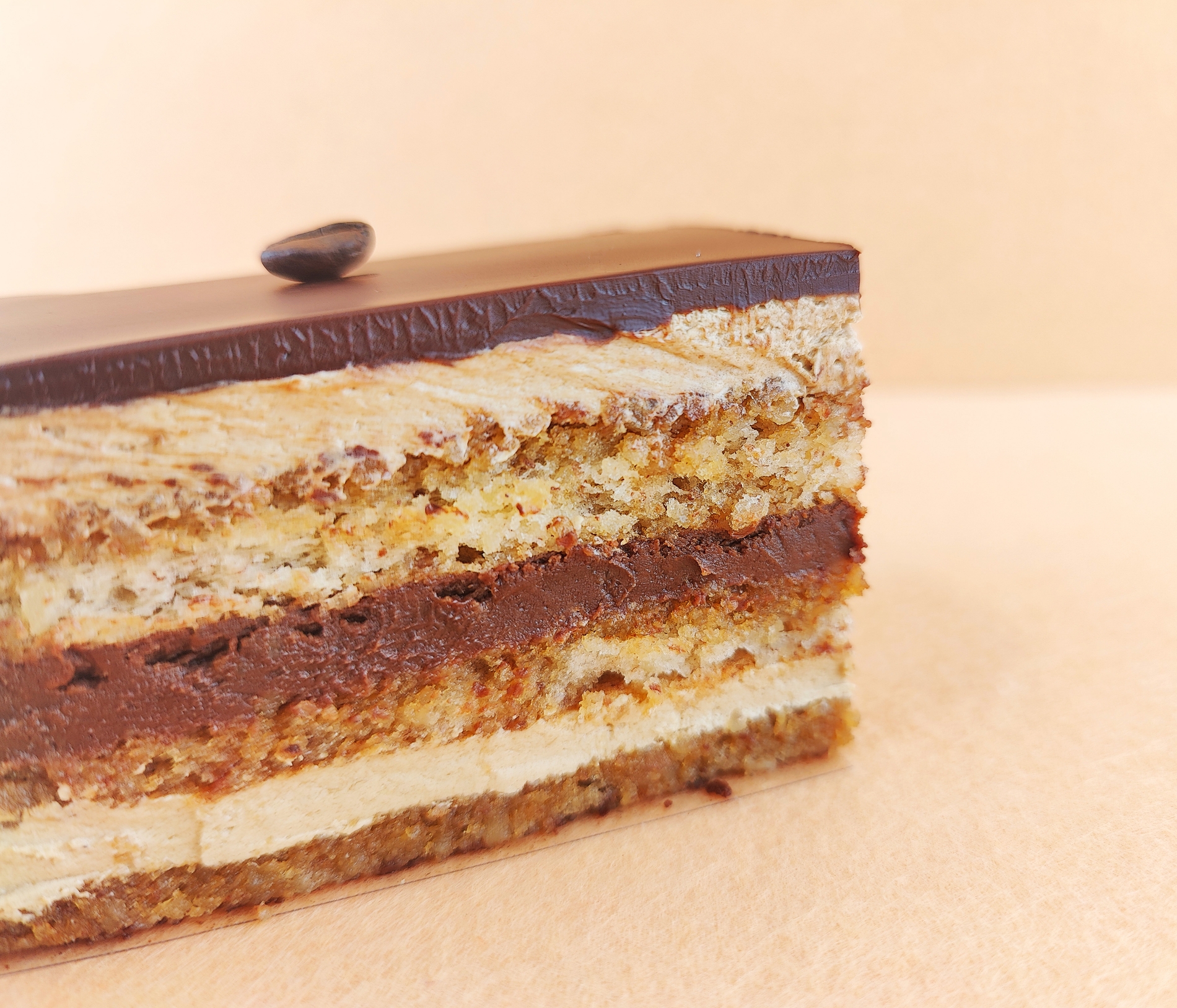 Primer plano de una porción rectangular de Tarta Ópera, destacando la textura lisa del glaseado de chocolate y la definición de las capas de bizcocho de almendra, crema de café y ganache de chocolate.