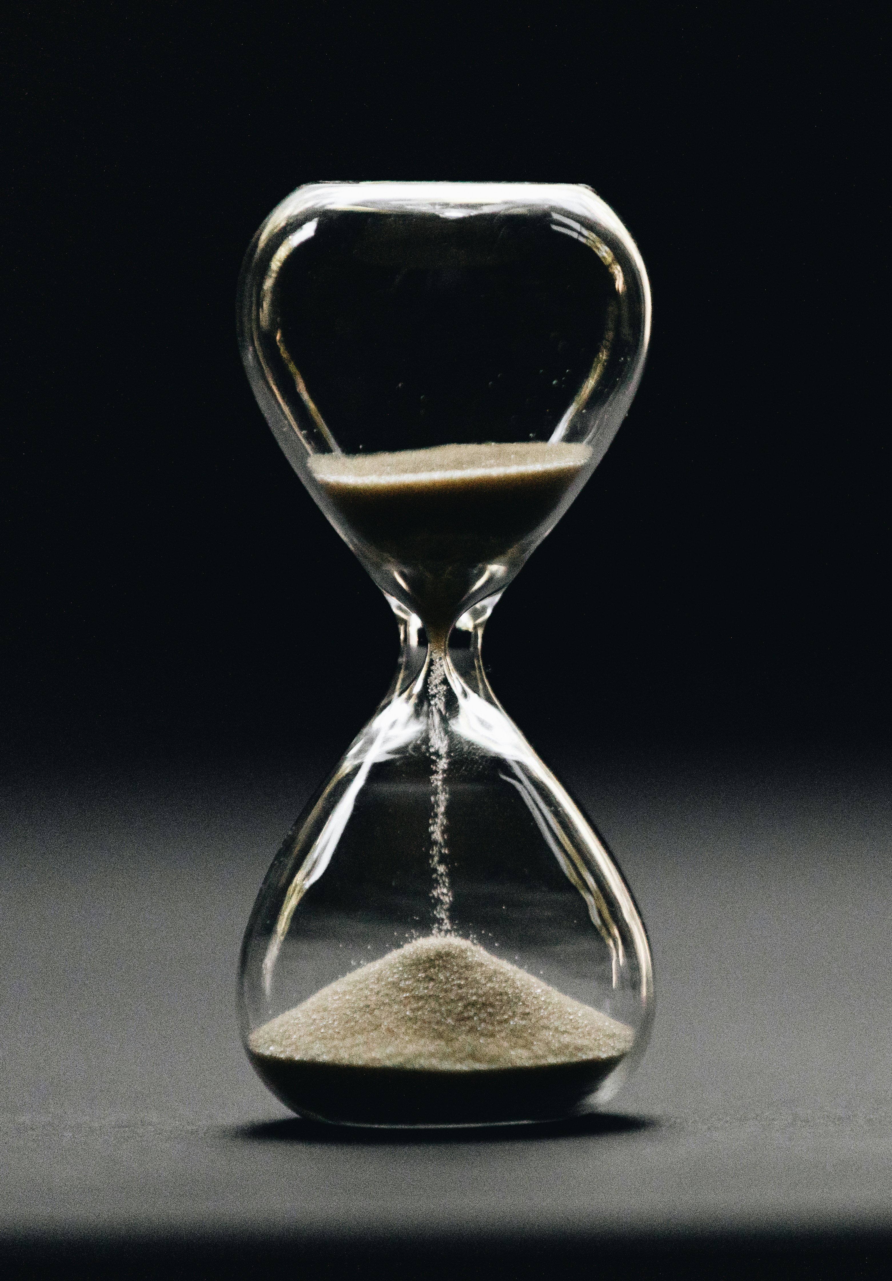 Reloj de arena de cristal con un fondo negro, derramando arena desde la parte de arriba hacia abajo estando más o menos a la mitad.