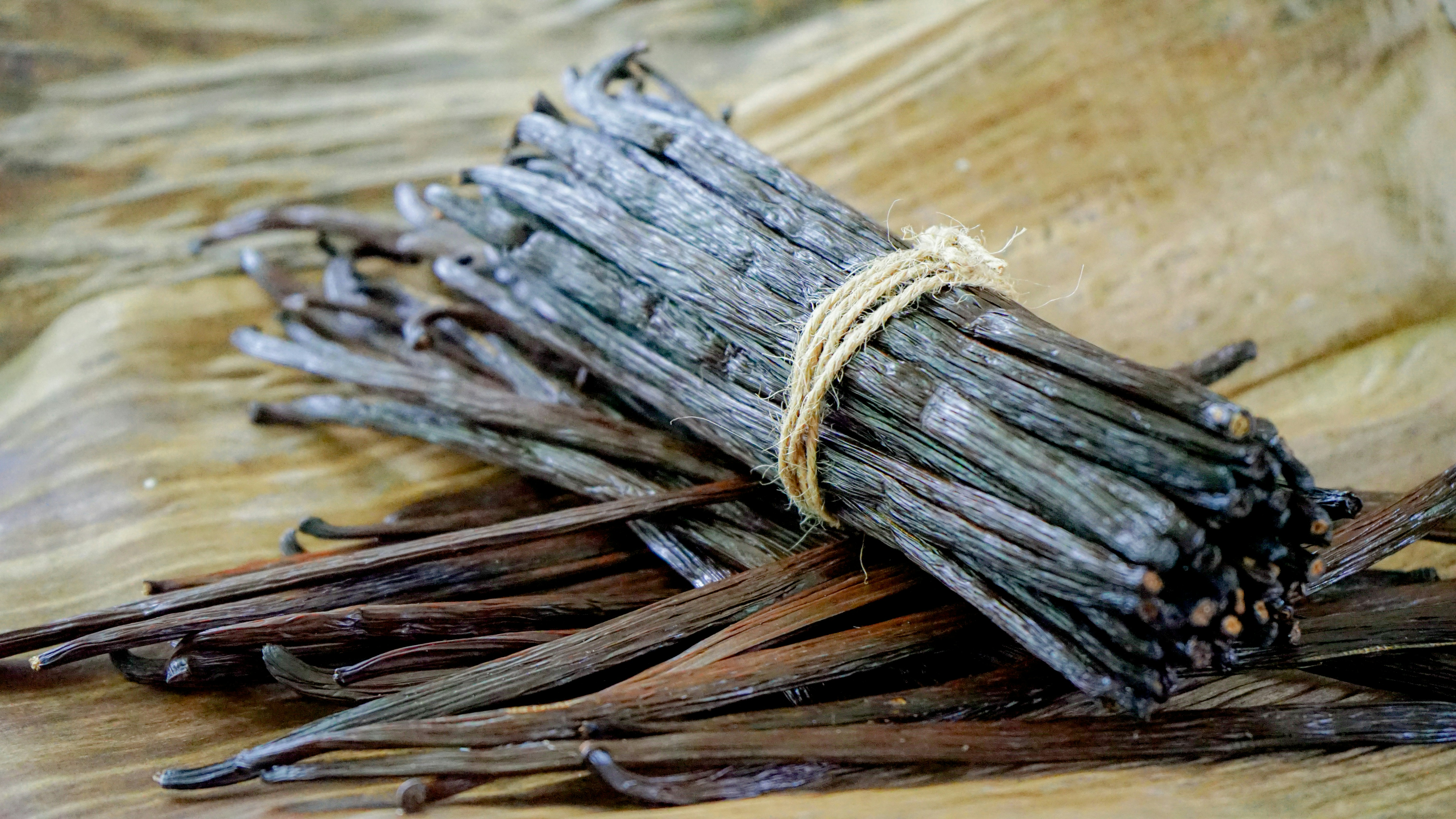 Varias vainas de vainilla, algunas atadas con un cordel y otras sueltas, sobre una hoja platanera seca